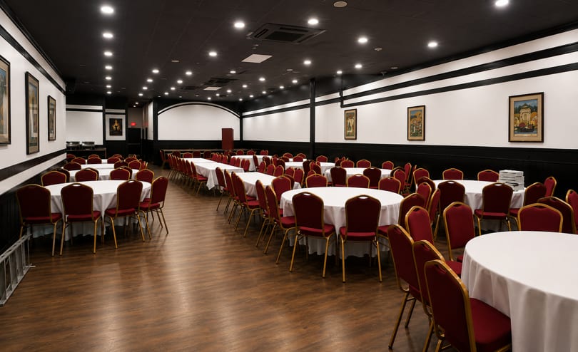Spacious banquet hall with round tables, white tablecloths, and red chairs, ready for an event.