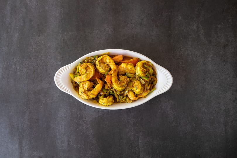 Curried shrimp with vegetables in a white oval dish on a dark gray surface.
