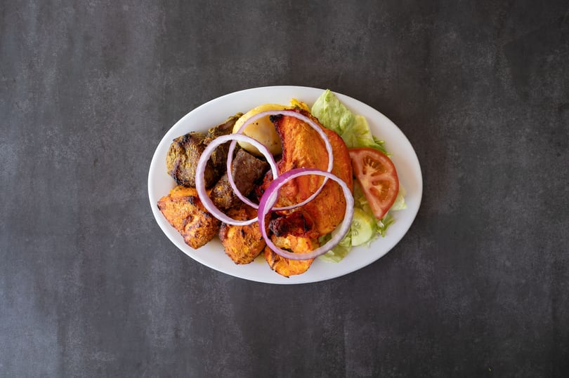 A white plate with grilled chicken, beef, shrimp, onions, and a side salad.