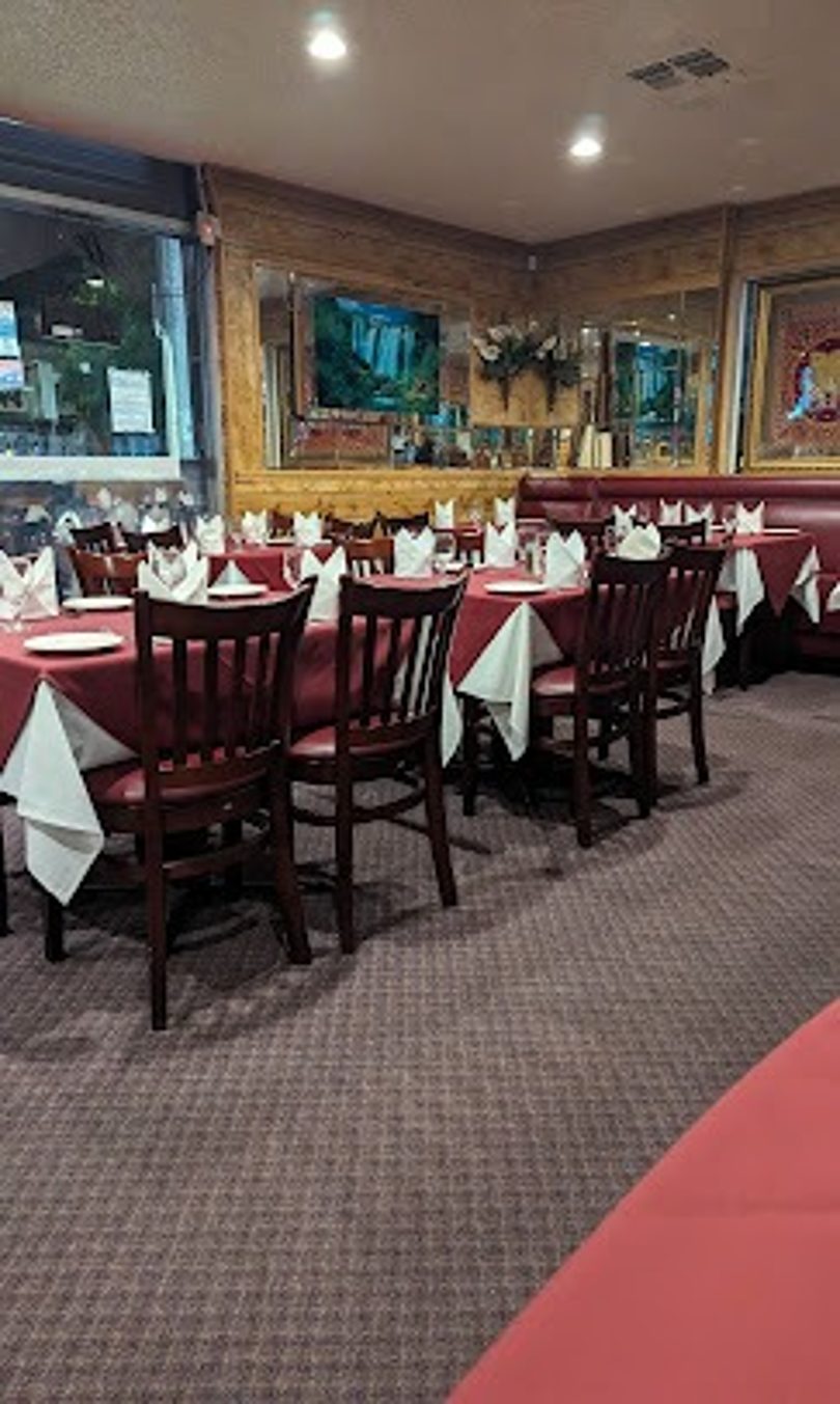 Restaurant dining room with red tablecloths, dark wooden chairs, and a TV on the wall.