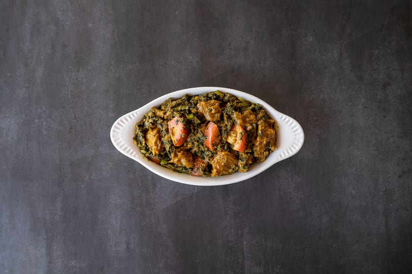 Overhead view of a white dish filled with a green curry, chicken, and tomato wedges.