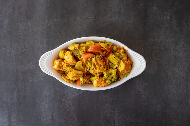 Colorful vegetable stir-fry with tofu, broccoli, tomatoes, and baby corn in a white dish.