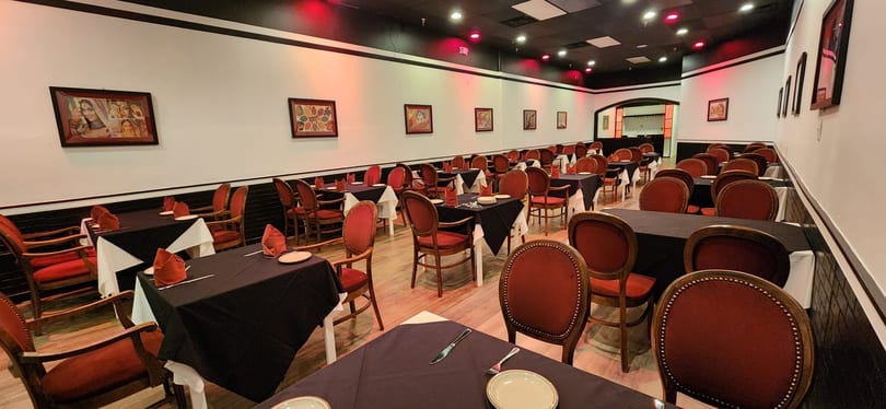 Empty restaurant dining room with black tablecloths, red chairs, and framed artwork on white walls.