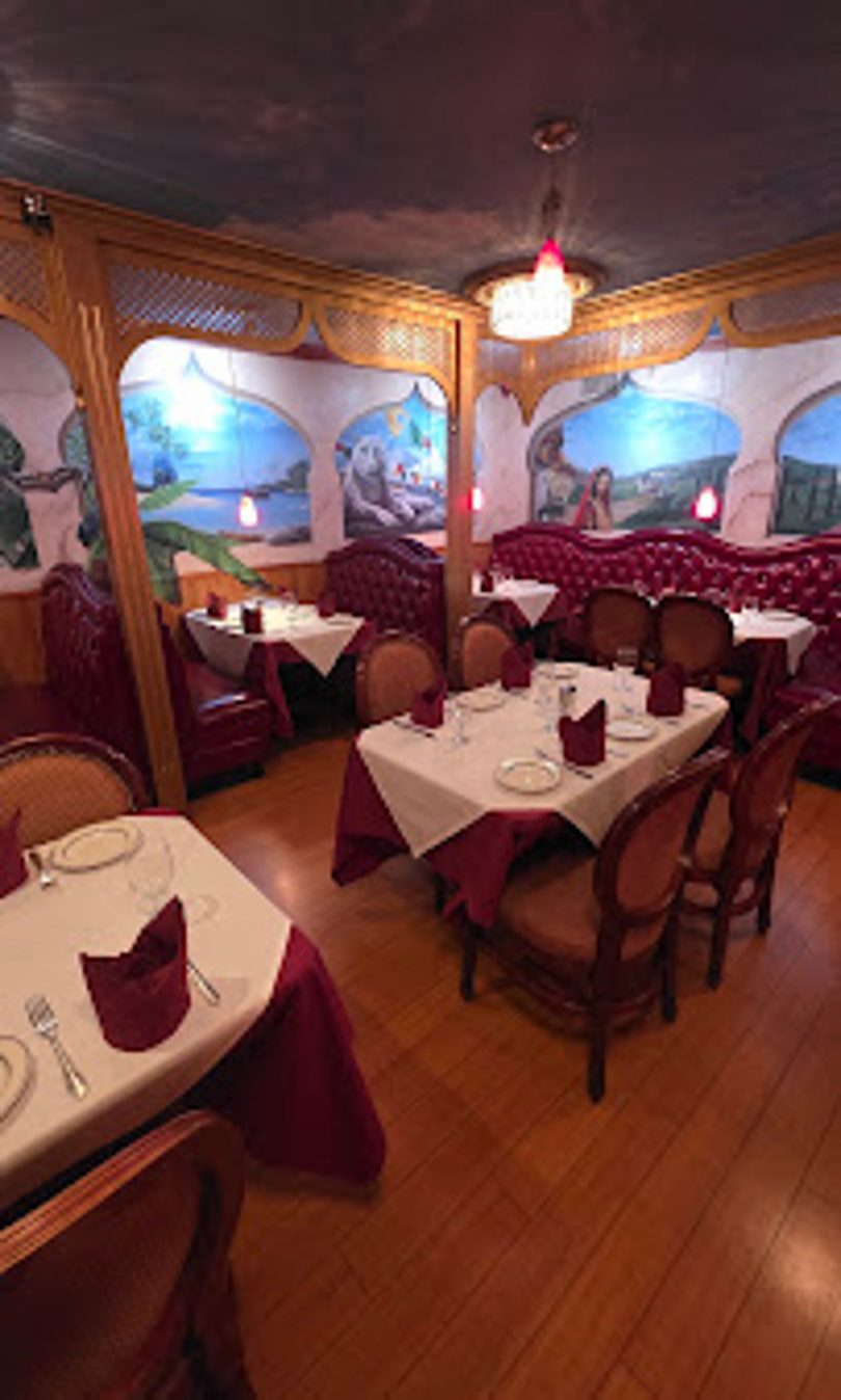 Empty restaurant dining room with red booths, white tablecloths, and wall murals of scenic landscapes.